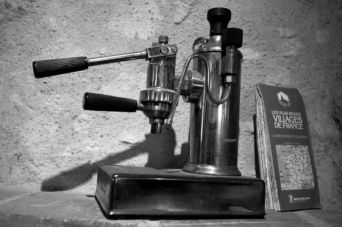 Espressor vechi cu manetă, din alamă, pe o masă de piatră